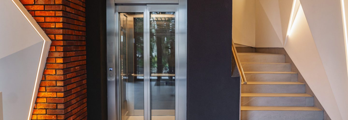 A modern entryway featuring a brick wall and a sleek glass door creating a contemporary aesthetic. The contrast between the warm, textured brick and the transparent glass adds interest to the space. Light filters through the door, illuminating the interior.